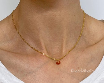 May include: A gold chain necklace with a small, orange carnelian stone pendant.