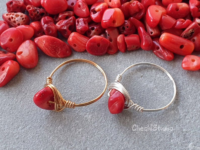 Puede incluir: Dos anillos envueltos en alambre con piedras de coral rojo. El anillo de la izquierda tiene una banda dorada y el anillo de la derecha tiene una banda plateada.