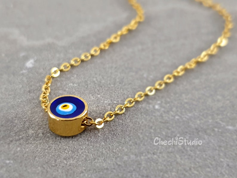 May include: A gold chain necklace with a blue and white evil eye charm. The charm is round and has a gold border.
