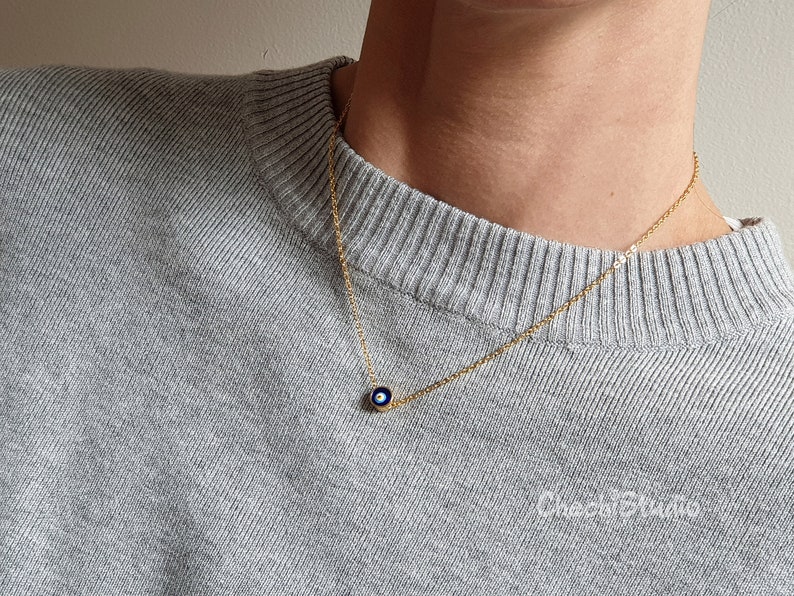 May include: A gold chain necklace with a small blue evil eye charm pendant.