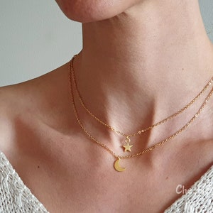 May include: A gold layered necklace with a crescent moon and star pendant. The necklace is on a person's neck.