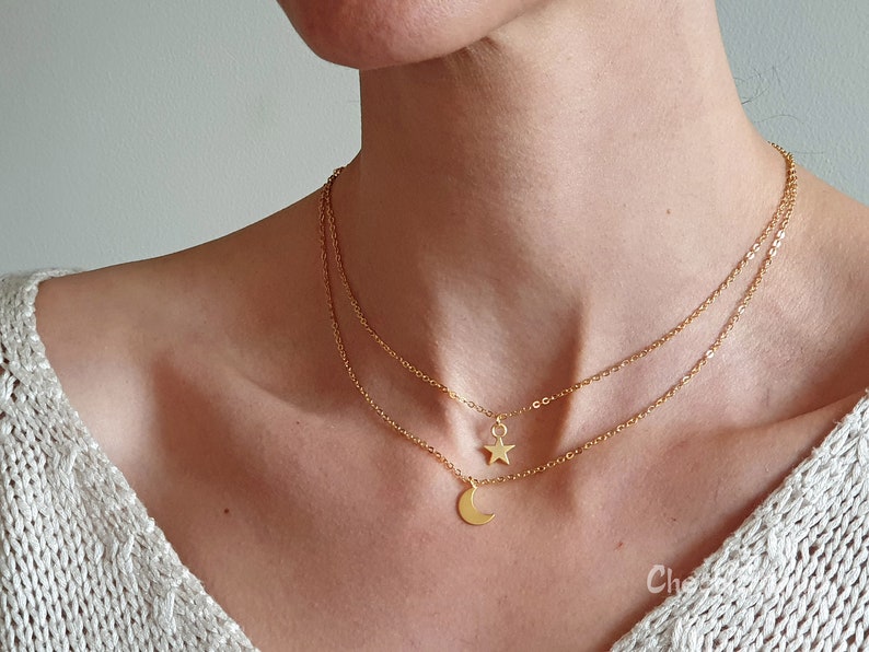May include: A gold layered necklace with a crescent moon and star pendant. The necklace is on a person's neck.