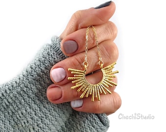May include: A gold necklace with a sunburst pendant. The pendant is made of thin, textured metal bars that radiate out from a central circle. The necklace is shown being held by a hand.