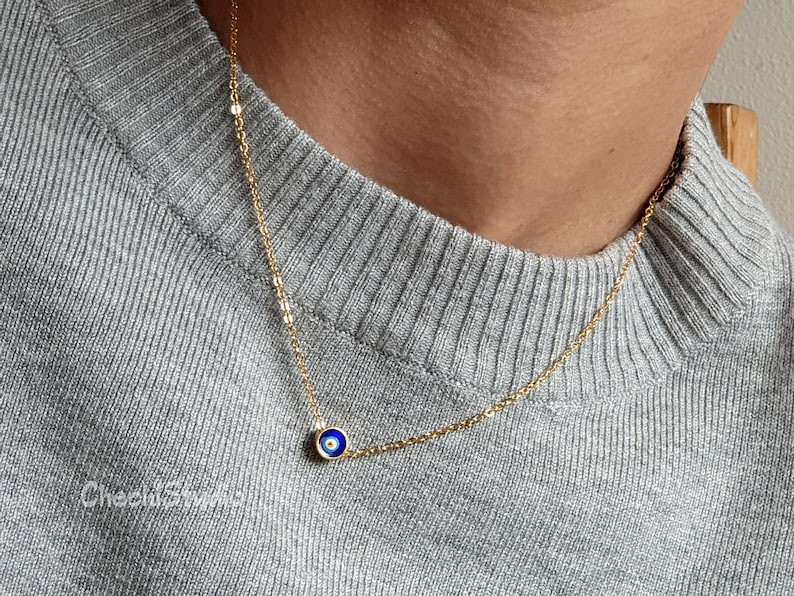 May include: A gold chain necklace with a small blue evil eye charm.