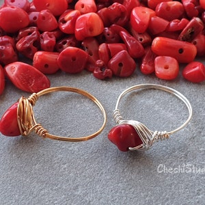 Puede incluir: Dos anillos envueltos en alambre con piedras de coral rojo. El anillo de la izquierda es de oro y el anillo de la derecha es de plata.