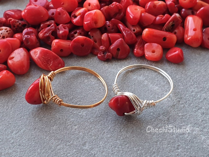 Puede incluir: Dos anillos envueltos en alambre con piedras de coral rojo. El anillo de la izquierda es de oro y el anillo de la derecha es de plata.