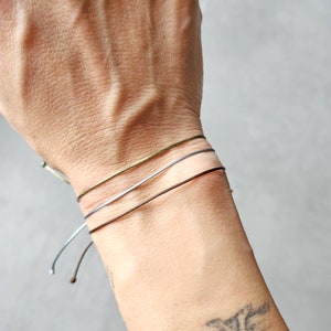 Può includere: Tre braccialetti sottili su un polso. I braccialetti sono verde, argento e marrone.