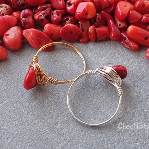 Puede incluir: Dos anillos envueltos en alambre con piedras de coral rojo. El anillo de la izquierda es de oro y el anillo de la derecha es de plata.