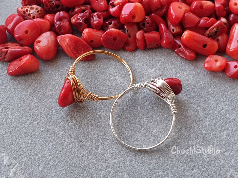 Puede incluir: Dos anillos envueltos en alambre con piedras de coral rojo. El anillo de la izquierda es de oro y el anillo de la derecha es de plata.
