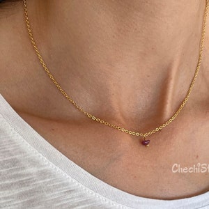 Op de afbeelding: Een delicate gouden ketting met een klein, donkerrood edelsteen hanger.