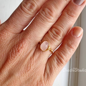 Puede incluir: Un anillo de alambre dorado con una piedra ovalada de color rosa claro.