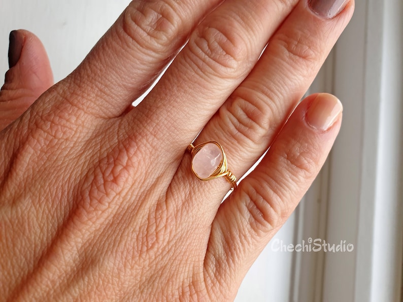 Puede incluir: Un anillo de alambre dorado con una piedra ovalada de color rosa claro.