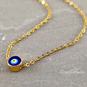 May include: A gold chain necklace with a small blue evil eye charm. The charm has a white center and a blue ring around it.