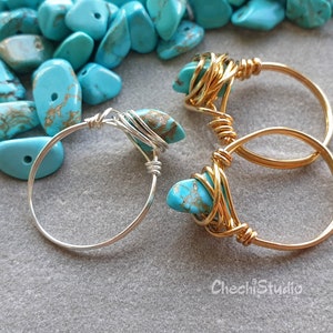 Op de afbeelding: Twee ringen met turquoise edelstenen, een met een zilveren band en een met een gouden band. De turquoise stenen zijn omwikkeld met draad.