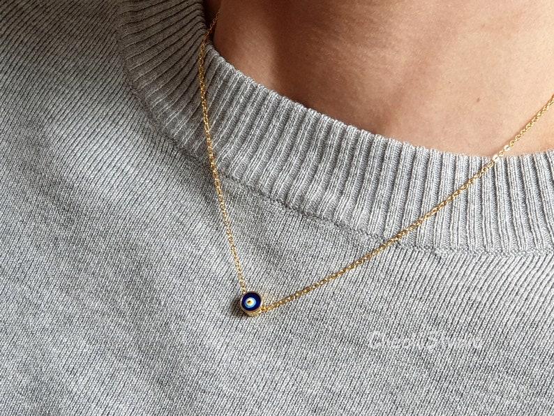 May include: A gold chain necklace with a small blue and white evil eye charm pendant.