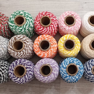 May include: A collection of 12 spools of baker's twine in various colors and patterns. The twine is white with a contrasting color stripe. The colors include red, green, pink, orange, yellow, brown, gray, black, purple, and blue.
