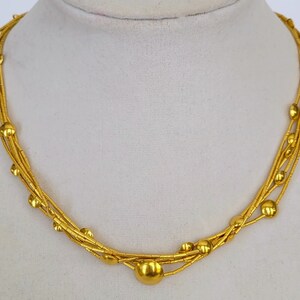May include: A gold necklace with multiple strands and round beads. The necklace is displayed on a white mannequin.
