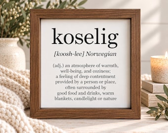 May include: A square wooden frame containing a white sign with black text that defines the Norwegian word koselig as an atmosphere of warmth, well-being, and coziness, including a feeling of deep contentment provided by a person or place.