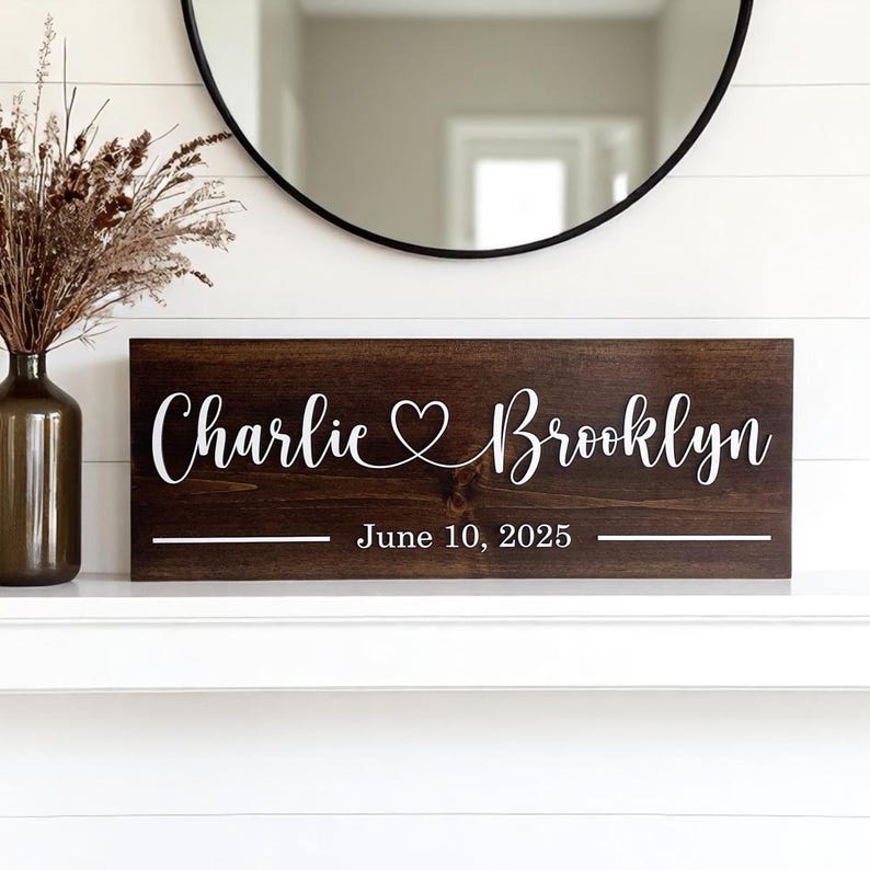 May include: A dark brown wooden sign with white lettering. The sign reads "Charlie &hearts; Brooklyn" with the date "June 10, 2025" below. The sign is rectangular and has a rustic, farmhouse style.