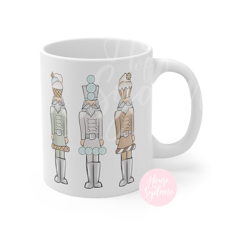 K&ouml;nnte beinhalten: Wei&szlig;e Keramiktasse mit drei Illustrationen von skurrilen Nussknackern. Jeder Nussknacker tr&auml;gt einen Hut und eine Uniform im Dessert-Stil in Pastellfarben. Die Tasse hat einen gebogenen Griff und eine gl&auml;nzende Oberfl&auml;che.