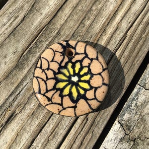 May include: A round ceramic ornament with a black and white floral design. The flower is yellow with a white center. The ornament has a hole at the top for hanging.
