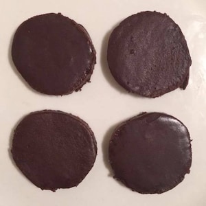May include: Four round, dark brown chocolate discs on a white surface.