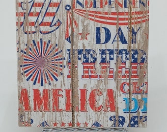 May include: A white wooden sign with red, white, and blue patriotic decorations and the text "Independence Day", "Freedom", "America", and "Celebrate" in a distressed font.