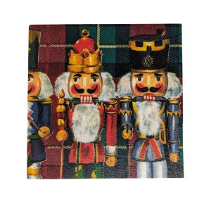 May include: Three nutcracker figurines with red, blue, and green accents stand in front of a plaid background. The nutcrackers are wearing traditional costumes and have painted faces.