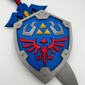 May include: A blue and silver plastic replica of the Master Sword and Hylian Shield from the Legend of Zelda video game series. The sword is attached to the shield.