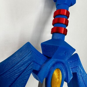 May include: A blue and gold 3D printed sword with red accents. The sword has a detailed design with a pointed tip and a handle with a textured surface.