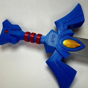 May include: A blue and gold plastic sword with a red and white handle. The sword has a triangular blade with a gold emblem on the front.