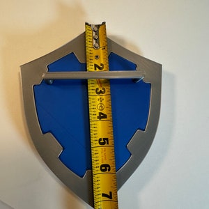 May include: A blue and silver shield-shaped wall decor with a metal handle. The shield is approximately 7 inches tall.