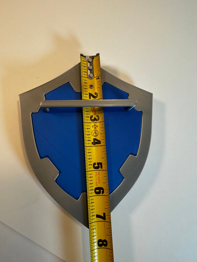 May include: A blue and silver shield-shaped wall decor with a metal handle. The shield is approximately 7 inches tall.