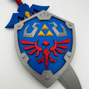 May include: A blue and silver plastic replica of the Master Sword and Hylian Shield from the Legend of Zelda video game series. The sword is attached to the shield.