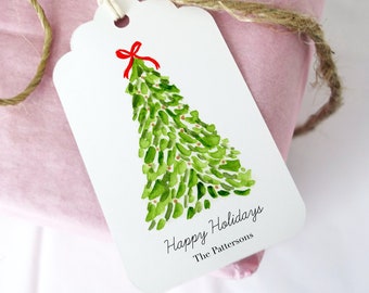 May include: A wrapped gift in pink paper tied with twine, featuring a white tag with a watercolor Christmas tree design. The tag reads "Happy Holidays" and "The Pattersons."
