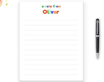 Può includere: Un blocco note bianco con pagine a righe e la scritta "a note from Oliver" in lettere colorate. Una penna nera è appoggiata accanto al blocco note. Graffette e forbici dorate, insieme a rose rosa, sono anche nell'immagine.