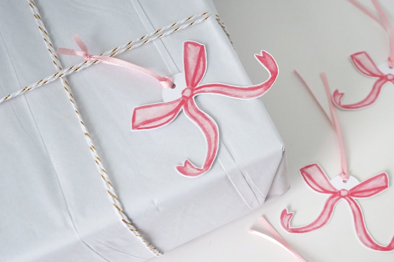 May include: A white gift box wrapped with gold twine and pink ribbon. The box is decorated with pink watercolour bow gift tags.