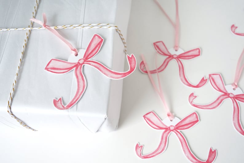 May include: Pink watercolour bow gift tags with a white circle in the centre. The tags are tied with pink ribbon and are ready to be attached to gifts.