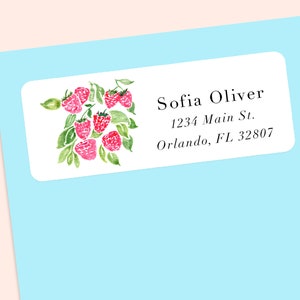 Puede incluir: Etiqueta rectangular blanca con una ilustración de acuarela de frambuesas rojas y hojas verdes. La etiqueta incluye el nombre "Sofia Oliver" y una dirección: 1234 Main St., Orlando, FL 32807. Sobre un fondo azul claro.