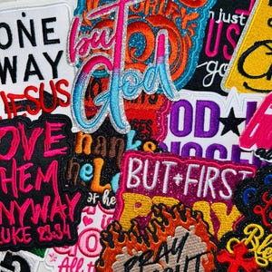 May include: A collection of colorful embroidered patches with various text designs. The patches feature phrases like "But God," "Love Them Anyway," and "But First Pray." The patches have glitter accents and a variety of fonts and colors.