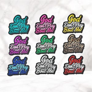 May include: Nine embroidered patches with the text "God Don't Play Bout Me" in various colors, including teal, pink, yellow, purple, green, gold, blue, white, and red. Each patch has a black border.