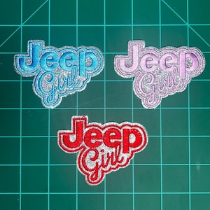 May include: Three embroidered patches with the words "Jeep Girl" in a cursive font. One patch is blue with silver glitter, another is pink with silver glitter, and the third is red with silver glitter. The patches are on a green grid.