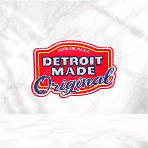 May include: A rectangular embroidered patch with a red background and yellow border. The text reads BORN AND RAISED in small white letters, DETROIT MADE in large white block letters, and Original in a large blue cursive script font.