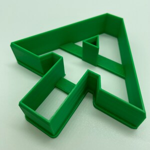 Puede incluir: Cortador de galletas de pl&aacute;stico verde en forma de la letra T.