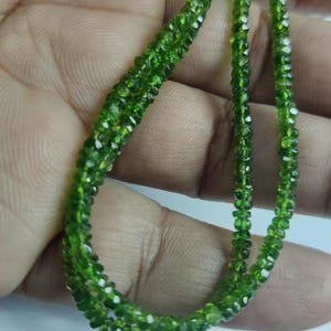 May include: A close-up of strands of faceted, bright green peridot beads. The beads are small and uniform, strung together. The colour is a vivid green, with a slight sparkle from the facets, suitable for a necklace or bracelet.
