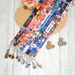 Peut inclure: Plusieurs lanières colorées avec des personnages et logos de films d'animation, dont "Elemental", "Les Indestructibles" et "Monstres & Cie". Chaque lanière a un fermoir en métal et un charm. Deux accessoires en forme de tête de Mickey Mouse scintillants sont également présents.