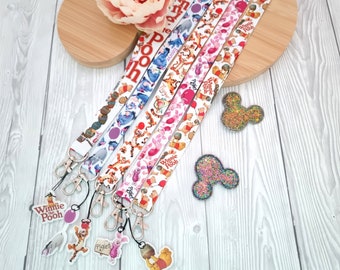 May include: Four fabric lanyards featuring Winnie the Pooh characters including Tigger, Piglet, and Eeyore, each with a silver metal lobster clasp and a hanging character charm. Two glittery mouse-ear shaped acrylic charms are placed to the side.
