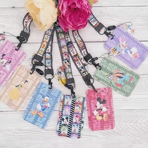 May include: A selection of Disney-themed lanyards and ID badge holders. The lanyards have a film strip design with various Disney characters. The ID holders feature characters such as Mickey, Minnie, Donald, and Daisy Duck in bright colours.