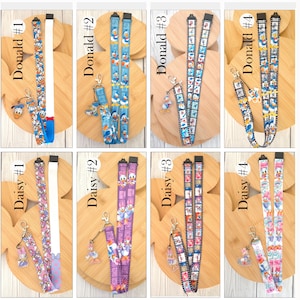 May include: A collection of eight fabric lanyards featuring Donald Duck and Daisy Duck character prints. Each lanyard includes a metal lobster clasp and a matching acrylic charm. The designs vary in color, including blue, purple, and white patterns.
