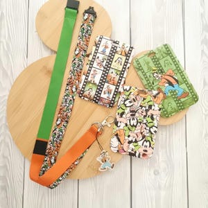 May include: A set of four colourful lanyards featuring a cartoon dog and mouse design. The lanyards are made of fabric and have a black clip. The lanyards are displayed on a wooden surface.